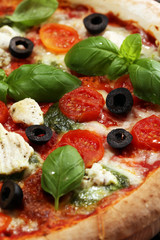 Pizza with tomatoes, mozzarella cheese, black olives and basil. Delicious italian pizza on wooden pizza board.
