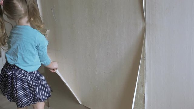 a little girl helps her mother to make repairs in the room, tears off the old Wallpaper from the wall
