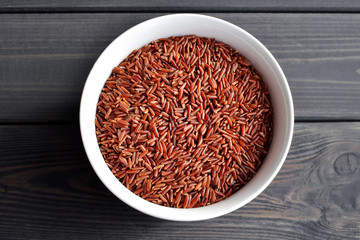 Fototapeta na wymiar Red rice in a small ceramic bowl against dark rustic wooden background