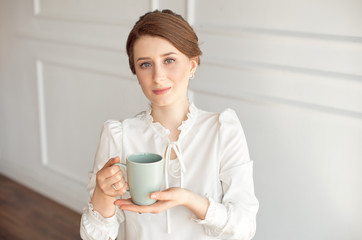 Attractive young woman in casual clothes is holding a cup, looking away and smiling, on white background.