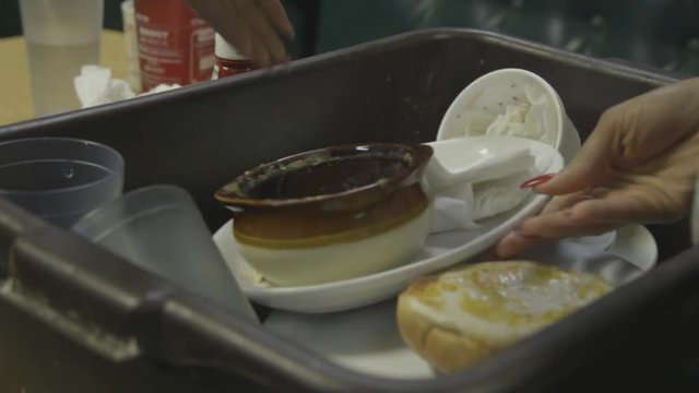 A hand with painted nails buses a table of dirty dishes and carries them away