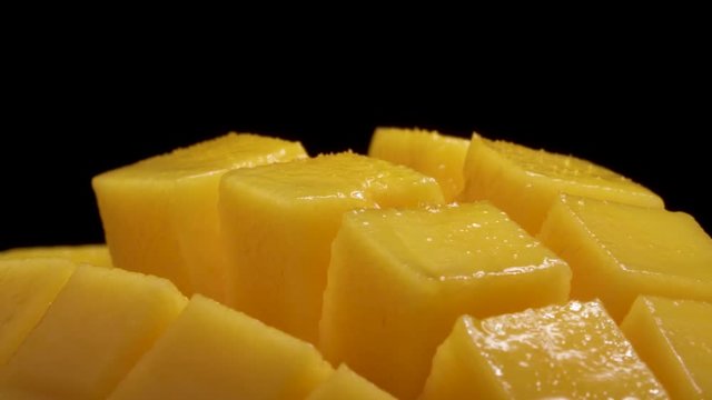 Macro shooting of a mango rotating on the turntable. Juicy sliced, hedgehog style served mango, isolated on the black background