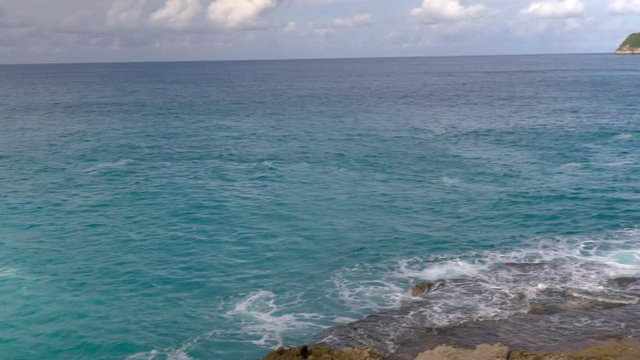 Panning shot from a rocky shoreline overlooking a vast blue ocean