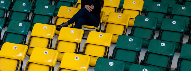The auditorium in the sports complex with plastic seats. A girl with a mobile phone in her hand is sitting on a yellow seat. Lonely sports spectator. Blank for website header or web banner.