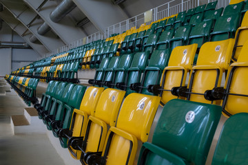 The auditorium in the sports complex with green and yellow plastic seats. Places for spectators of a sports match indoors. The territory of football fans.