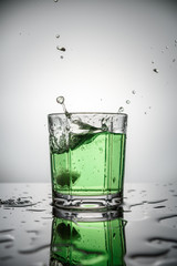 vertical image splash of green water in glass and drops on table on grey background