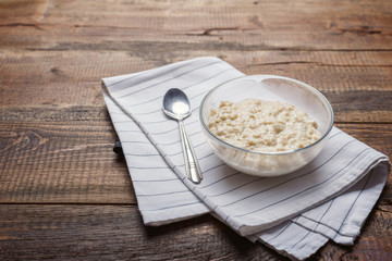 Oatmeal with spoon on white napkin on brown wooden background, healthy Breakfast