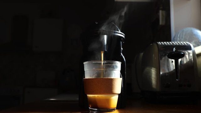 Video of steaming coffee espresso machine flowing into a glass cup. 
Harsh sun side lighting with dark left-hand side.
4k 60fps interpreted at 30fps.