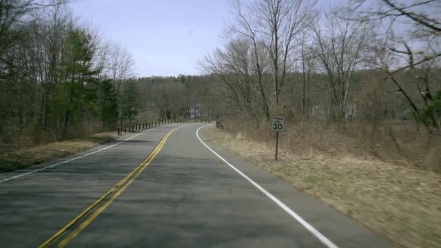 a fast drivers pov from a car windshield down a rural road leading up to a small pond