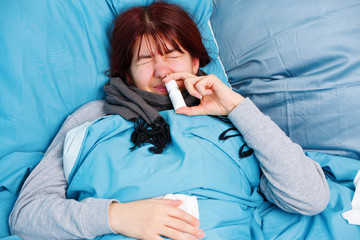 Photo of sick woman using nasal spray lying on bed