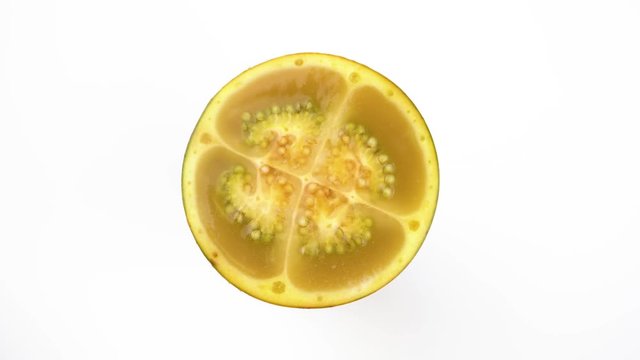 Top view from above of a naranjilla fruit sliced in half rotating on the turntable, isolated on the white background.