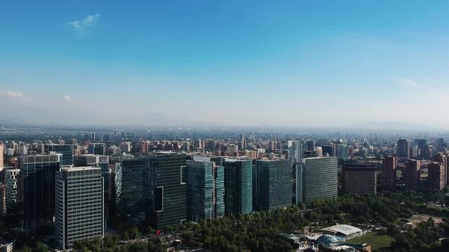 View from a drone of some tall modern buildings near a big park with all the city behind on a clear sky day.