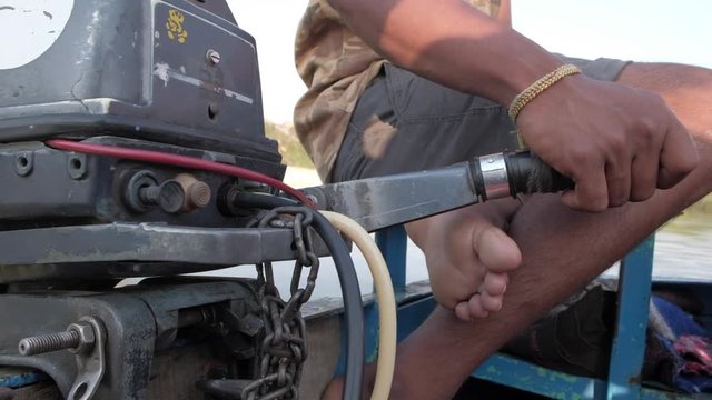 Closeup handheld shot of the boatman operating the engine of a powered boat in Hampi, Karnataka on a river 