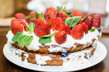 Strawberry cake in cream and mint leaves on the table in a plate, on the background of a teapot with tea, in light colors, close-up with a blurred background.