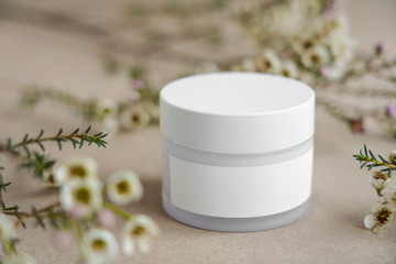 White  round cosmetic jar on a beige background decorated with white flowers