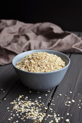 Rolled oats in ceramic bowl on dark wooden table with texture
