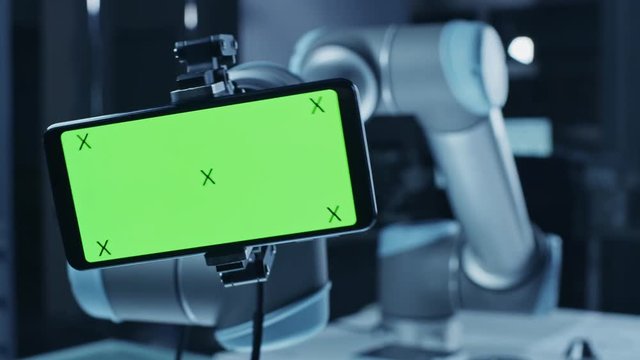 Robot Arm Holding Green Mock-up Screen Smartphone in Landscape Mode, Smoothly Moving into Focus. Industrial Robotic Manipulator End Effector Holds Mobile Phone with Chroma Key Display. 