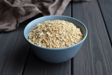 Rolled oats in ceramic bowl on dark wooden table with texture