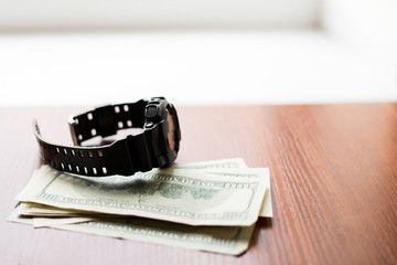 Time is money. One hundred dollars and black watch on wooden table.