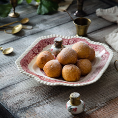 Homemade small round ball donuts sprinkled with powdered sugar on vintage plate