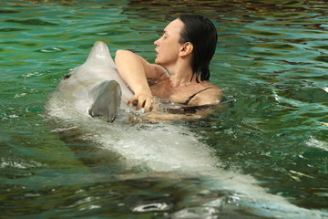 Fototapeta premium Young woman is scratching the dolphin's belly in the pool, swimming with dolphins