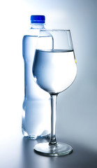 Plastic bottle with water and a glass filled with water. Backlight. White blue tone. Side view.