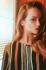 Fototapeta premium Beautiful portrait of a girl in profile. Girl stand near the window with blinds. Beautiful portrait of a girl. Photos with fashionable toning
