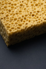 Close up view of cleaning sponge, mesh structure pattern on black surface. Yellow sponge close-up.