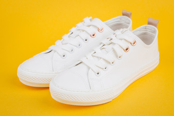 Pair of new white sneakers on yellow background