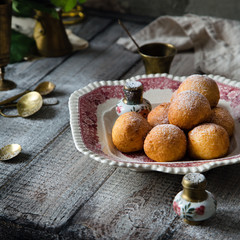 Homemade small round ball donuts sprinkled with powdered sugar on vintage plate