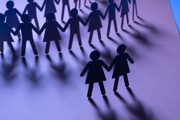 Black paper figure of a female couple in front of a crowd of paper people holding hands on blue...