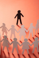 Paper human figure standing in front of paper people holding hands on red surface. Bulling,...