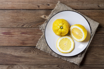 Three trendy ugly organic lemons on a white plate on a wooden natural painted background. Horizontal orientation. Copy space