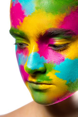 The young girl's face is painted with colored paints. Close up. white background. Spots of yellow, green, blue and purple paint on the model's skin.