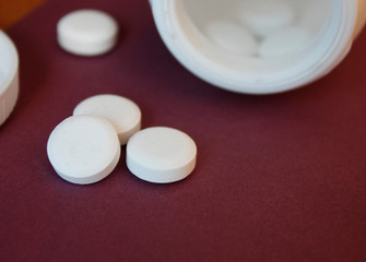 Fototapeta na wymiar white capsules poured out of the container, red, burgundy background, close-up