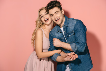 smiling girlfriend in pink dress and handsome boyfriend in denim shirt hugging