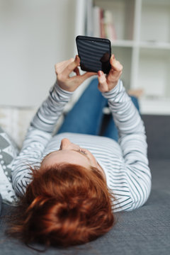 Redhead woman lying on her back reading her mobile