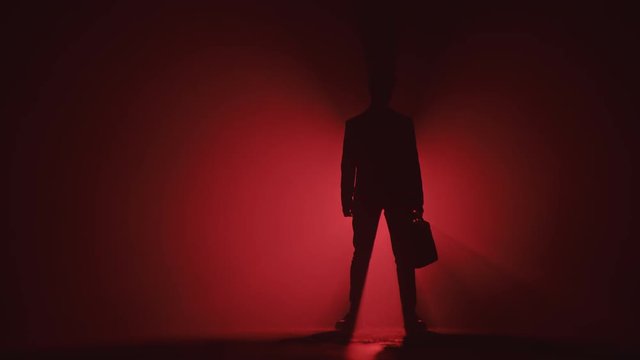 Man with a Suitcase Stands on Red Background in Silhouette. Businessman On Red Background concept.