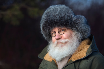 Smiling senior caucasian man in vintage eyeglasses poising against dark nature. Closeup portrait of...