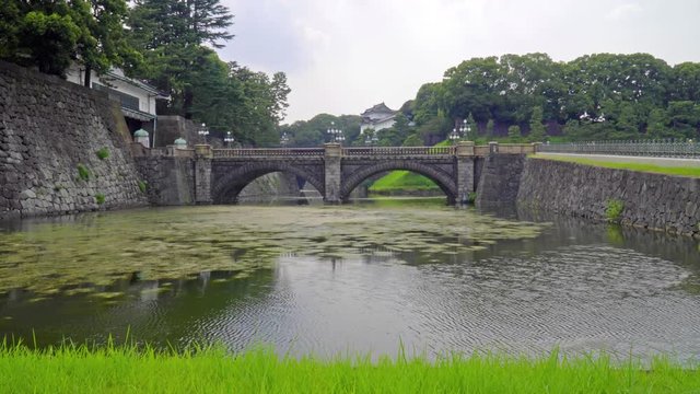 Long view from the edge of the pond in front of the Imperial Palace, Toyko, Japan with a view of the double arch stone bridge at the Palace's main gate. lily​ pads