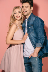 smiling girlfriend in pink dress and handsome boyfriend in denim shirt hugging and looking away