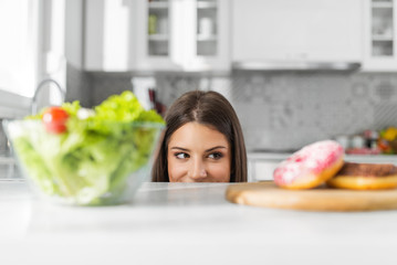 Diet. Dieting concept. Healthy Food. Beautiful Young Woman choosing between Salad and Sweets