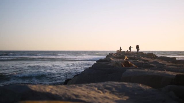 Beautiful, calm, sunset in San Diego, shooting down a jetty with people and waves crashing alongside it.