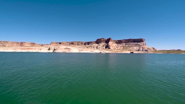 As viewed from out in the turquoise waters of Lake Powell, Page, Arizona a speedboat in the distance races past the sandstone buttes
