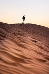 Fototapeta na wymiar Dark silhouette of a man walking at the desert dunes. Dawn time