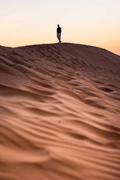 Dark silhouette of a man walking at the desert dunes. Dawn time