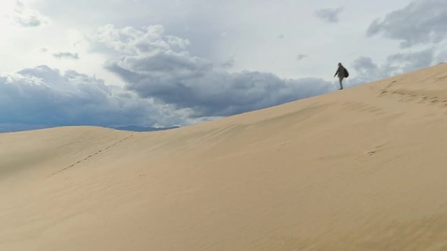 Slow motion of a lady with a backpack walking along the ridge of a high, distant sand dune