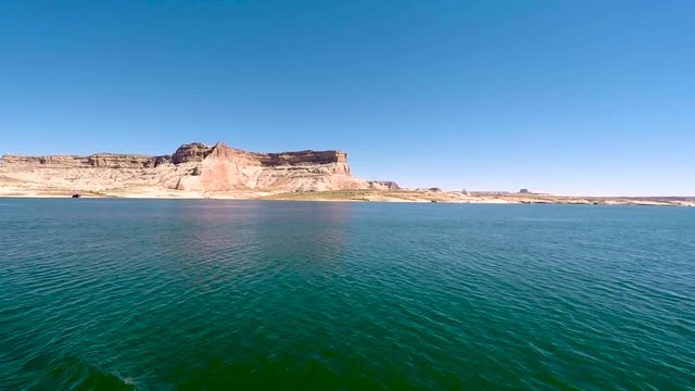A houseboat cruises through the turquoise waters of Lake Powell, Page, Arizona passing the sandstone buttes that ring the lake shore.