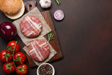 Hamburger ingredients raw cutlet, tomatos, lettuce, bun, cheese, cucumbers and onion on rusty background