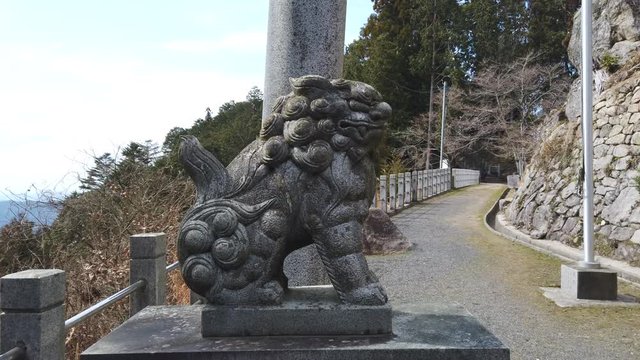 A zoom shot on a Fu Dog (guardian deity) statue at a Shinto Shrine on a rural mountain trail in Japan.